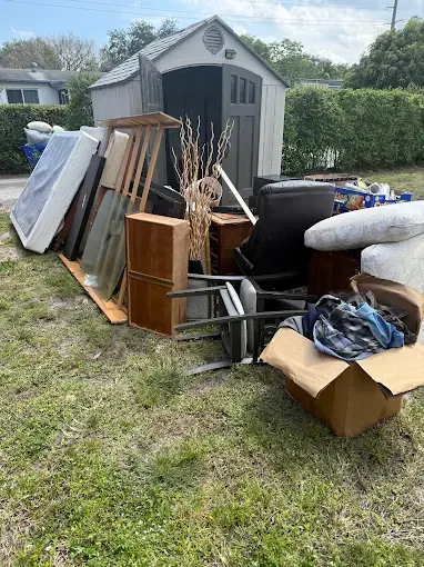 Old furniture, boxes and a mattress stacked in a yard beside a shed